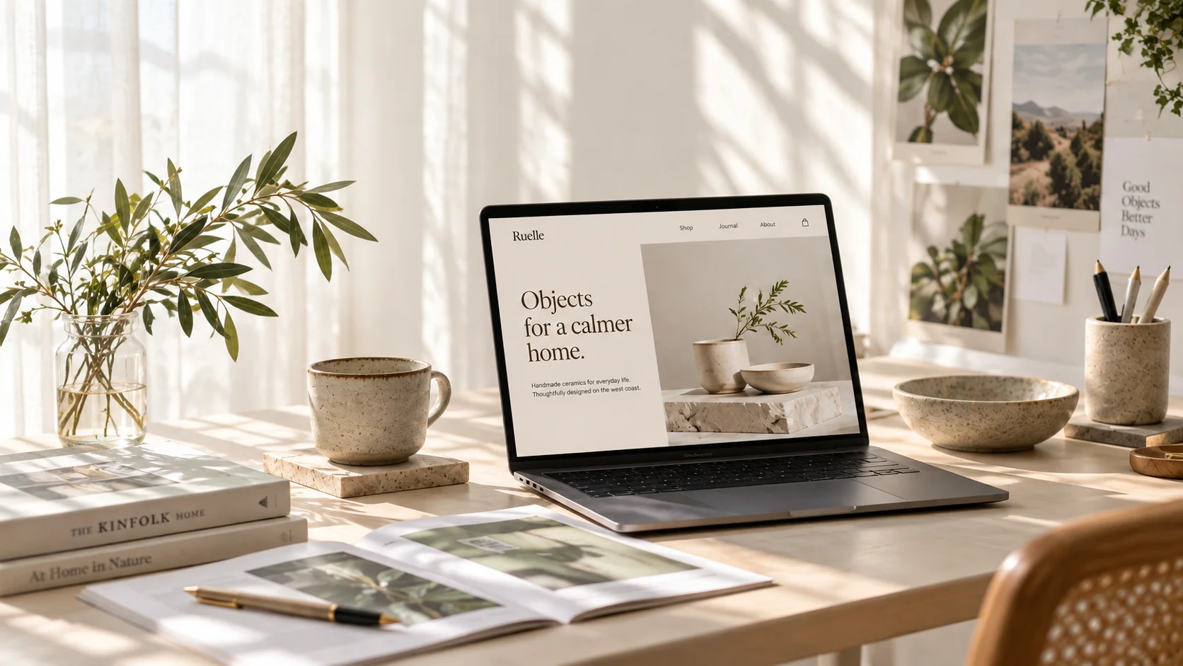A ceramics website on a laptop in a sunlit studio, surrounded by handmade pottery and olive branches.
